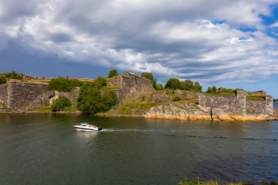 A scenic view of Suomenlinna Fortress with a boat passing by on a sunny day.