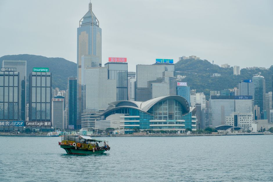 A traditional boat sailing in front of Hong Kong's modern skyline across Victoria Harbor.