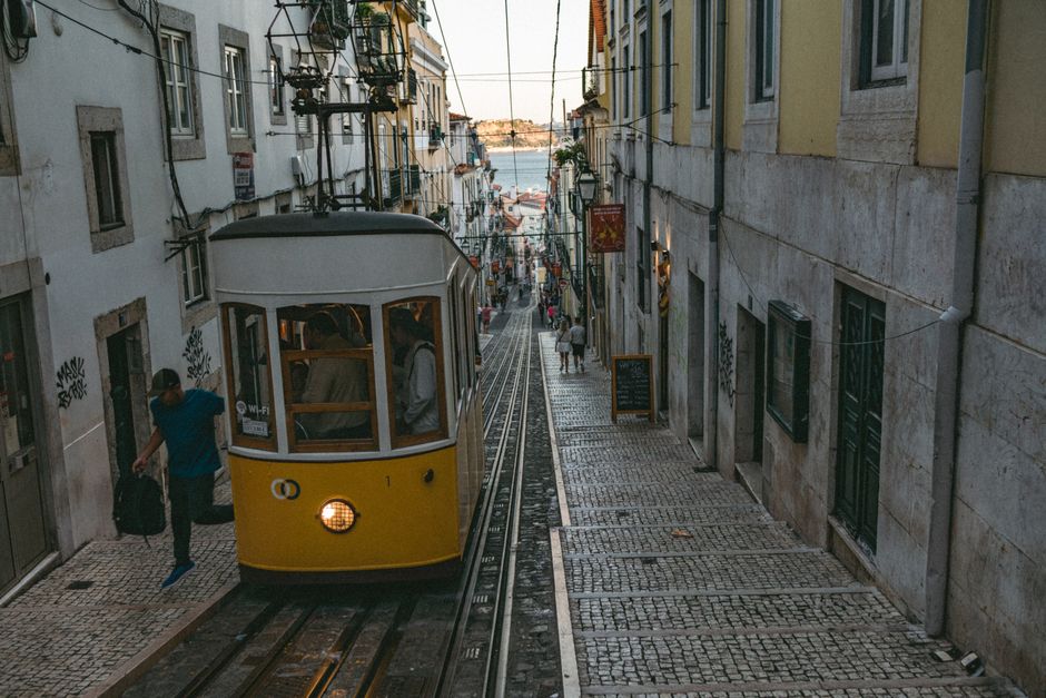 Vintage tram navigates a quaint cobblestone street in Lisbon, Portugal, capturing urban charm.